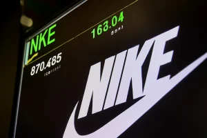 Nike stock trading screen showing live price, volume, and logo at stock exchange in sharp focus.