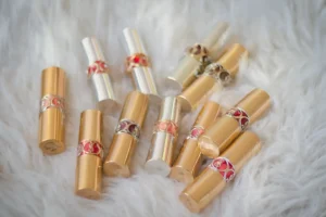 Twelve luxurious engraved lipstick tubes in gold and silver cases displayed on soft white fur background.